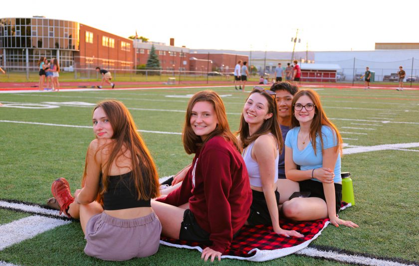 five students sitting on football field watching the sunset