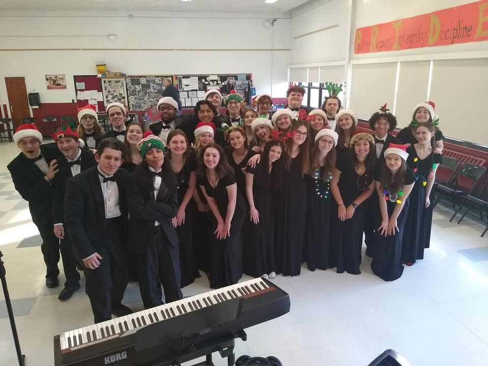 The Choralaires students dressed in black suits and dresses with holiday hats