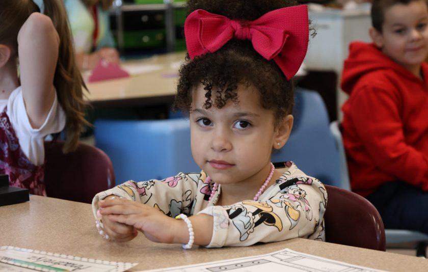 student sitting at table with a big red bow in her hair