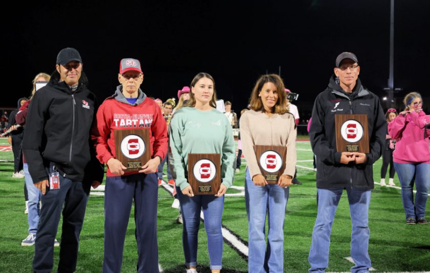 Athletic Director and four adults holding their hall of fame plaques on the football field with the school band behind them