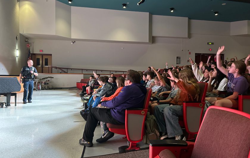 Officer stands in front of students in auditorium raising their hands