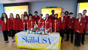 students wearing the same red blazer with the SkillsUsa patch standing together behind it candles at a ceremony 