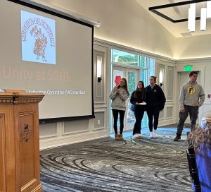 four students standing in front of a projector giving a presentation