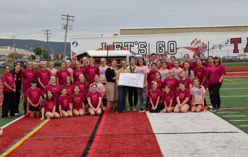 students in red soccer uniforms surrounding coaches and representative accepting a donation in the form of an oversized check