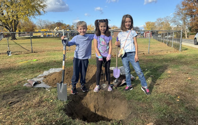 three second grade students standing in front of a hole dug for a tree