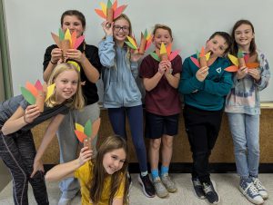 seven students holding colored paper turkeys they crafted with hershey kisses in them