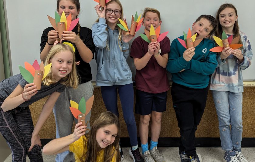 seven students holding colored paper turkeys they crafted with hershey kisses in them