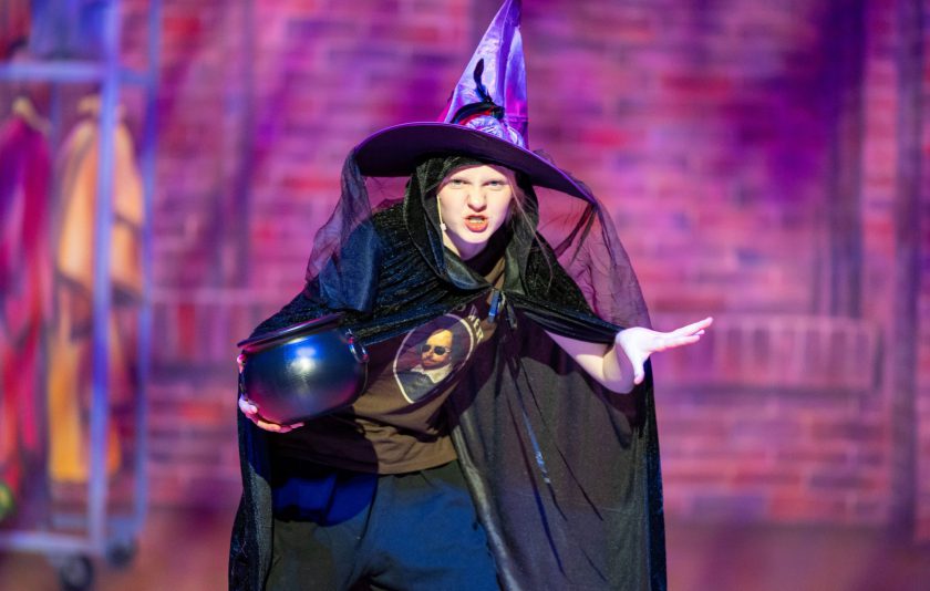 drama student in purple witches hat hunched over