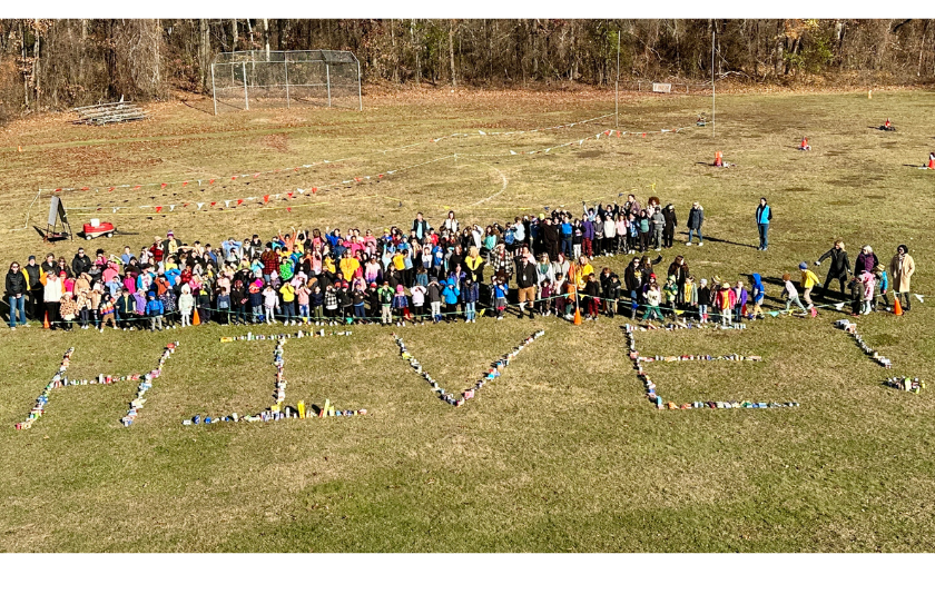 students and teacher and staff standing behind food donations that spell out HIVE on an outdoor field of the school