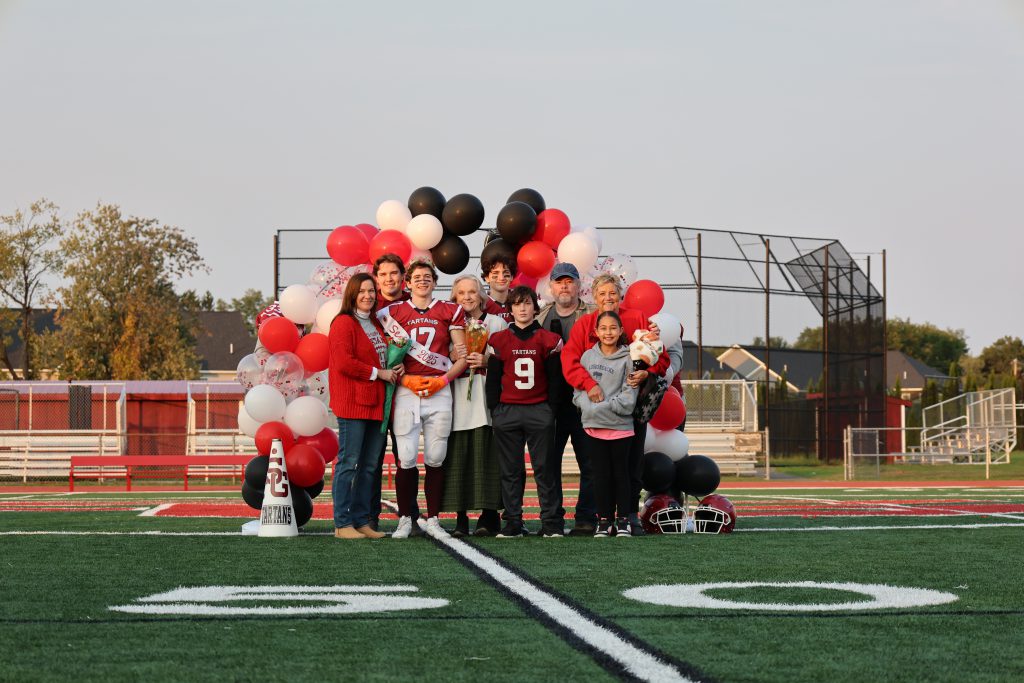 family standing together at family night on the football field in front of an archway of balloons