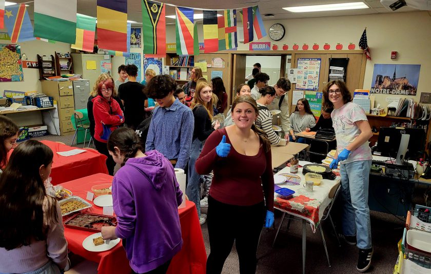 student gives thumbs up while other students smile for camera or eat pastries