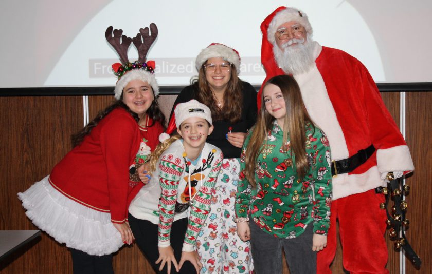 santa, Mrs. Claus, and a student dressed as a reindeer with other students dressed in festive attire