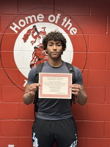 student stands proud while holding up Athlete of the Month Certificate