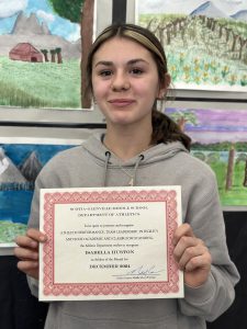 student proudly smiles holding the certificate for athlete of the month