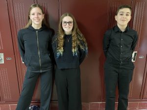 three students dressed in black and leaning against the wall