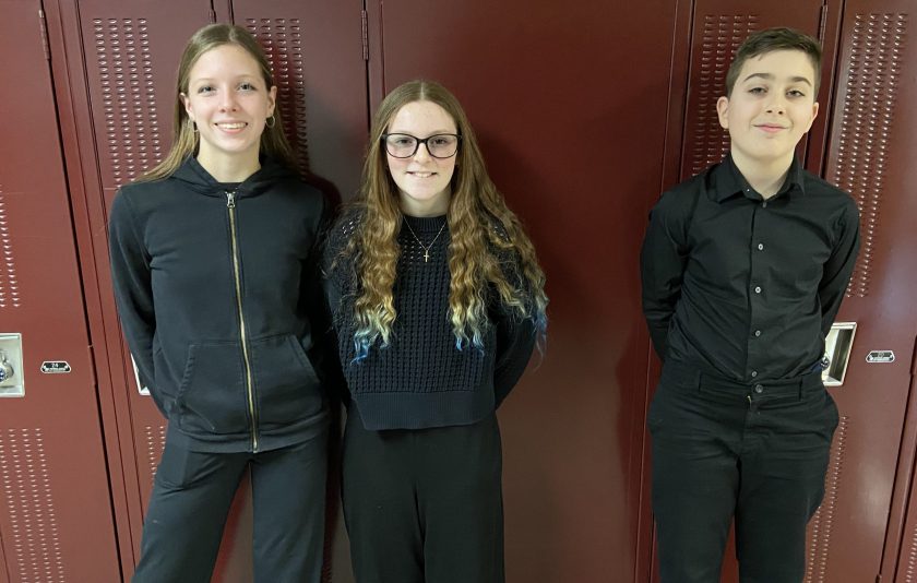 three students dressed in black and leaning against the wall