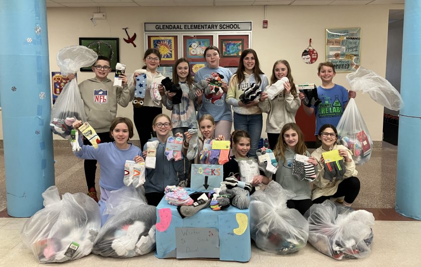 students gather together with socks in their hands and bags of socks all around them