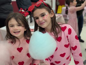 two students holding cotton candy wearing pink sweaters with red hearts