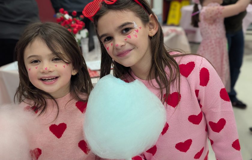 two students holding cotton candy wearing pink sweaters with red hearts