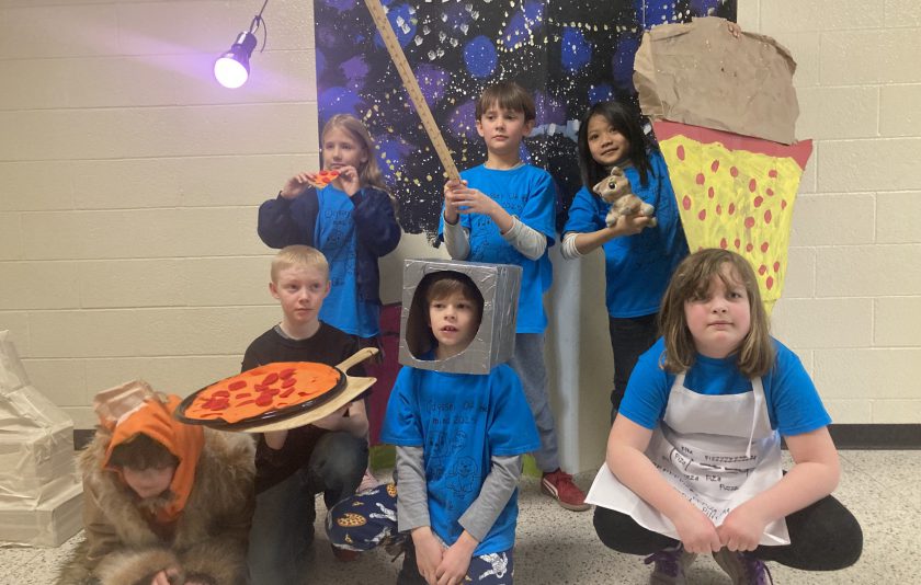 students standing with oversized props like a pizza and ice cream cone and light on a stick